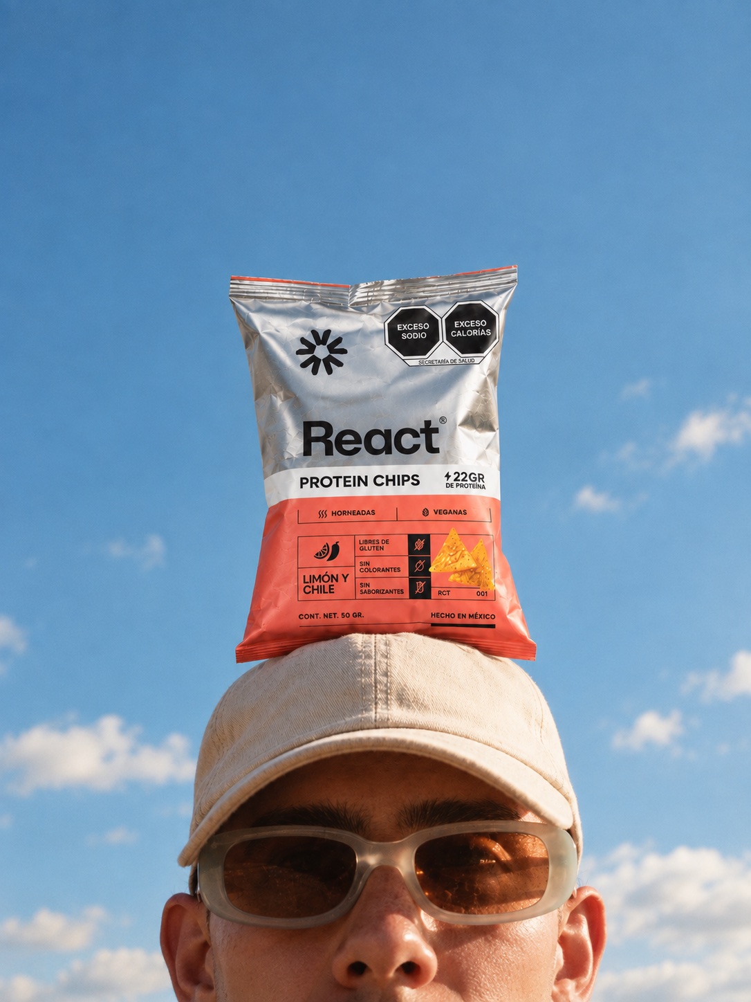 Bolsa de REACT Protein Chips balanceada sobre una gorra, cielo azul de fondo